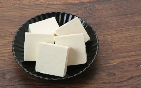 Kilka kostek białego tofu na czarnym talerzu. Czy tofu można mrozić? Tak, po rozmrożeniu zmienia teksturę, stając się bardziej gąbczaste.