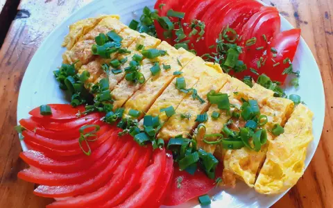 Pyszne koreańskie śniadanie: pokrojony omlet z jajek posypany szczypiorkiem, podany z plasterkami pomidora.