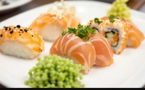 Talerz z różnorodnym nigiri sushi z łososiem, posypane sezamem i ozdobione natką pietruszki. Obok porcja zielonego wasabi.