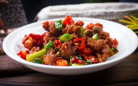 Chrupiący kurczak po kantonsku z papryczkami chili i zieloną cebulką na białym talerzu.