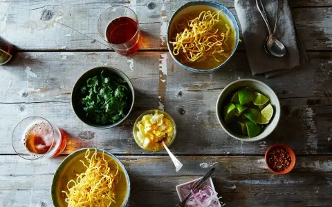 Dwa miseczki khao soi, świeża kolendra, limonki, jajko na twardo, czerwona cebula i płatki chili na drewnianym stole.