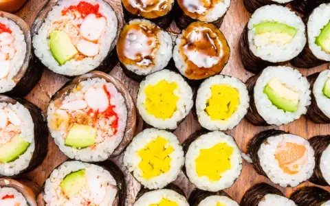 Różnorodne rolki sushi: grubsze futomaki z krewetkami i awokado, cieńsze hosomaki z łososiem, awokado, żółtą rzodkwią i polane sosem.