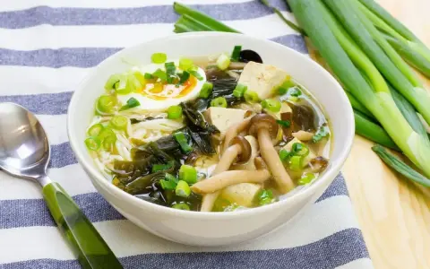 A miska pełna aromatycznej zupy miso z tofu, grzybami, wodorostami, jajkiem i szczypiorkiem.