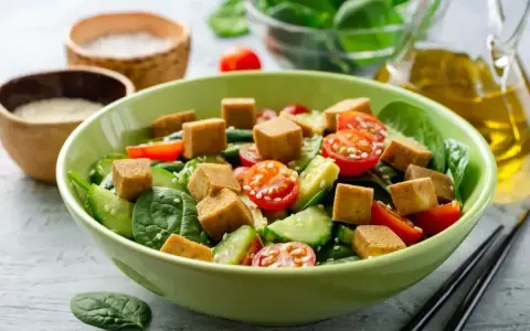 Sałatka ze szpinakiem, pomidorkami, ogórkiem i kostkami **butter tofu**, posypana sezamem.