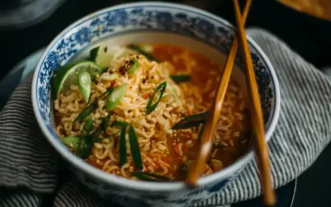Aksamitny makaron lau thai w misce z niebieskimi zdobieniami, udekorowany szczypiorkiem, chili i limonką.