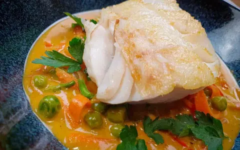 Aromatyczny curry z dorszem, podane z groszkiem i marchewką w kremowym sosie.
