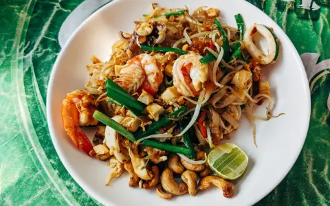 Pad thai z krewetkami, kalmarami, kiełkami i orzechami nerkowca. Widać też kawałek limonki, idealne pad thai składniki.