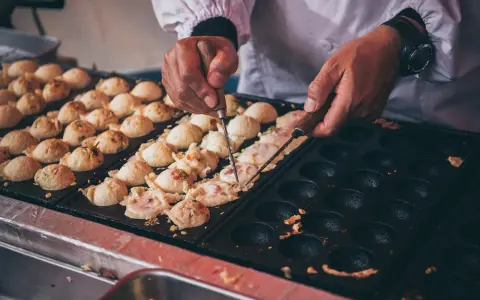Ręce obracają kulki takoyaki na specjalnej patelni. Ten prosty takoyaki przepis jest w trakcie realizacji.