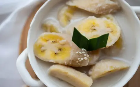 Kawałki banana w mleku kokosowym, ozdobione liściem pandanu i sezamem. Pyszny tajski deser.