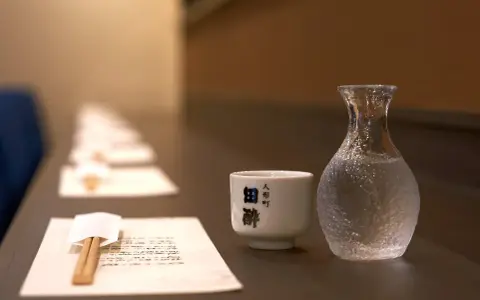 Sake ile procent? Delikatna czarka i karafka z sake czekają na degustację. W tle rząd nakryć.