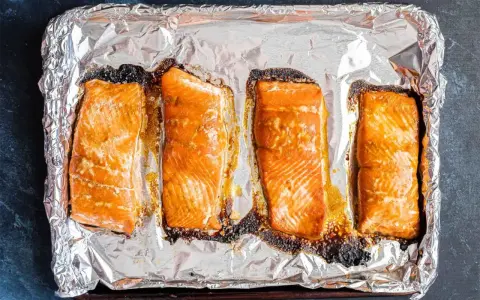 Cztery kawałki pieczonego łososia na folii aluminiowej. Idealny łosoś do sushi, lekko przypieczony na brzegach, zachęca do przygotowania.