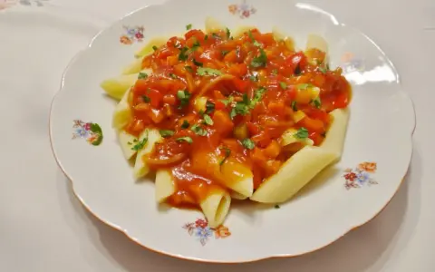 Penne z aromatycznym, słodko-kwaśnym sosem warzywnym, posypane świeżą natką pietruszki.