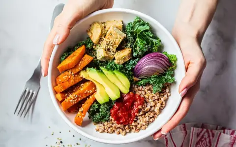 Pyszny bowl z kaszą, pieczonym batatem, awokado, tofu i czerwoną cebulą, polany pikantnym sosem do bowla.