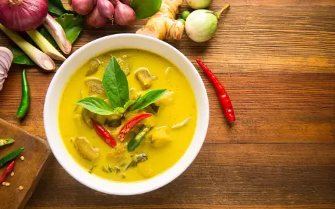 Aksamitne tajskie curry z tofu, ozdobione świeżą bazylią i papryczkami chili, otoczone składnikami jak galangal i trawa cytrynowa.