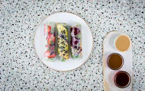 Trzy świeże spring rolls z owocami i warzywami, podane z sosami.