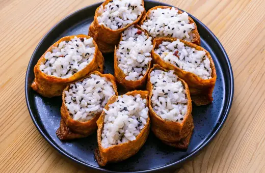 Tofu inari z ryżem i czarnym sezamem na czarnym talerzu.