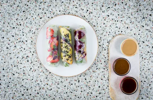 Trzy świeże spring rolls z owocami i warzywami, podane z sosami.