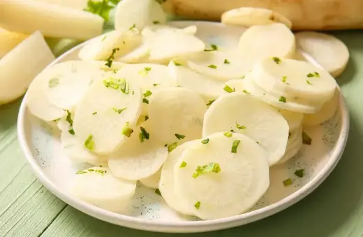Plasterki białej rzodkwi, czyli daikon, posypane zielonymi ziołami na talerzu.