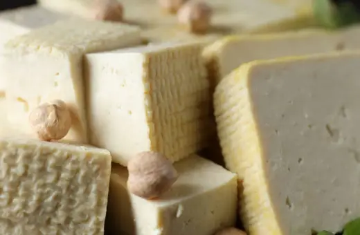 Kawałki miękkiego tofu ułożone obok siebie, niektóre z nich mają kratkowaną fakturę. Kilka ciecierzycy dodaje uroku.