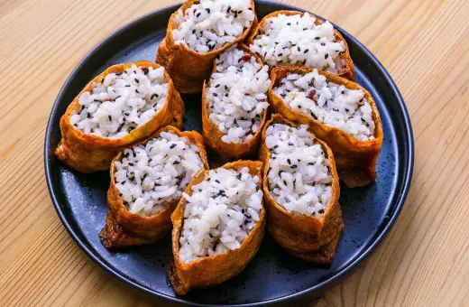 Tofu inari z ryżem i czarnym sezamem na czarnym talerzu.