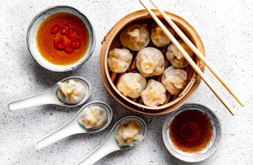 Pyszne dim sum w bambusowym parowniku, podane z sosem chili i sosem sojowym. Trzy pierożki na łyżeczkach zachęcają do spróbowania.