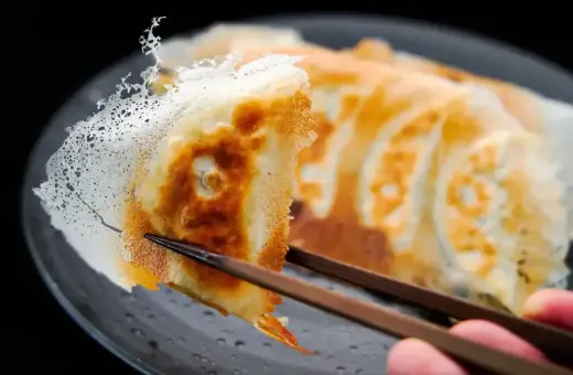 Chrupiące pierogi gyoza z delikatną, koronkową panierką, podniesione pałeczkami.