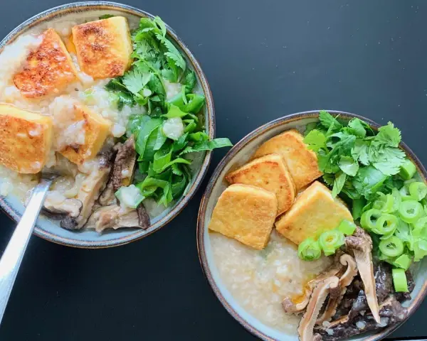 Dwie miseczki aromatycznego congee z chrupiącym tofu, grzybami i świeżymi ziołami.