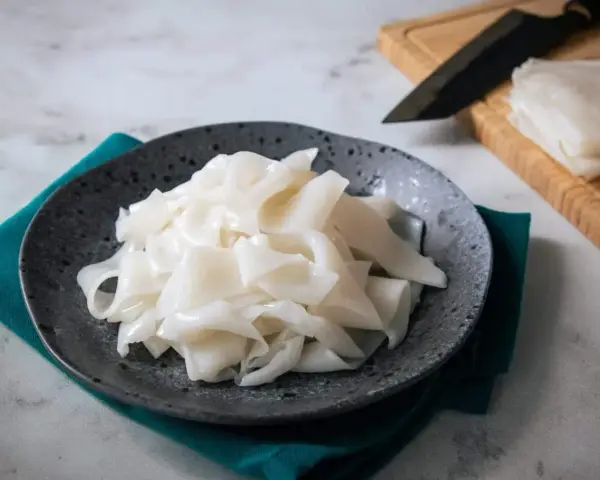 Płaski, biały makaron ryżowy na talerzu, gotowy do przygotowania pysznych dań. Szukasz inspiracji? Sprawdź makaron vermicelli przepisy!