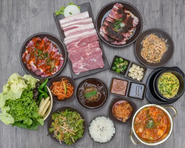 Obfity zestaw do korean bbq: surowe i marynowane mięso, kimchi, sałatki, ryż i dodatki.