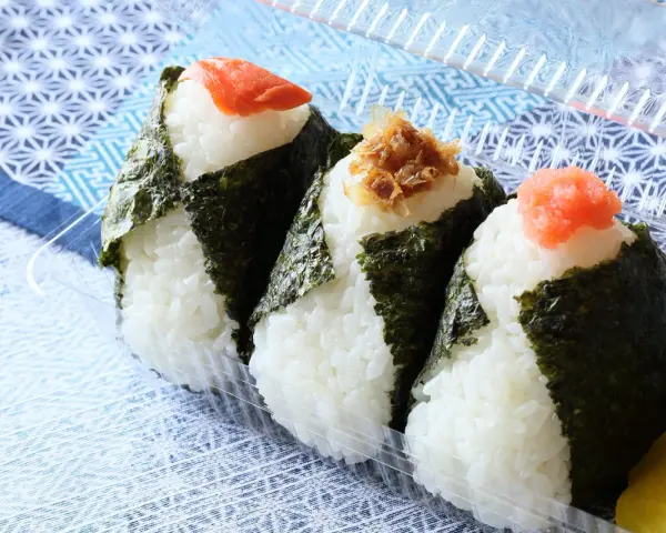 Trzy onigiri z ryżem, zawinięte w nori, z łososiem, tuńczykiem i ikrą na wierzchu. Idealne na przekąskę.