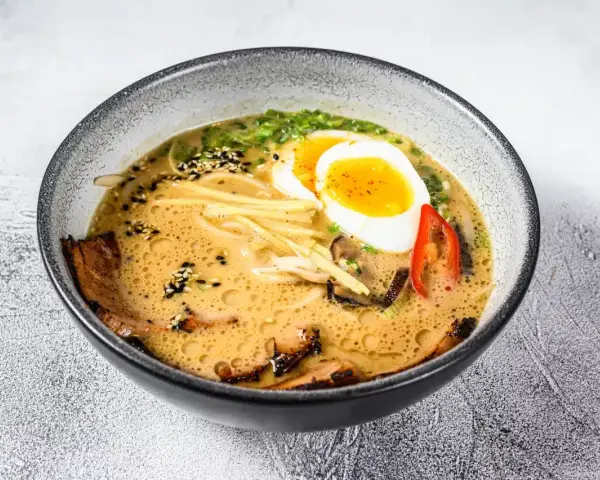 Miseczka aromatycznej zupy ramen z jajkiem na pół, plastrami mięsa, grzybami i szczypiorkiem.