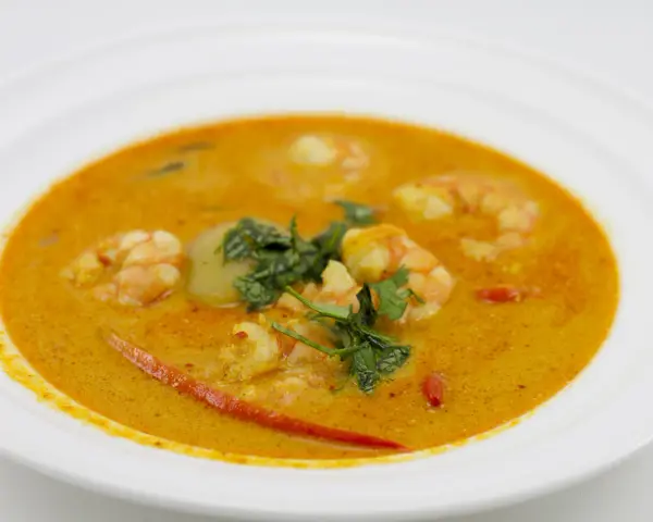 Aksamitna zupa tom yum z krewetkami, świeżą kolendrą i kawałkami chili na białym talerzu.