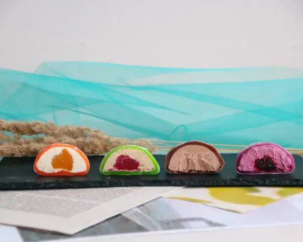 Cztery kolorowe mochi: pomarańczowe, zielone z malinami, czekoladowe i fioletowe z jagodami. Różne rodzaje słodkości.