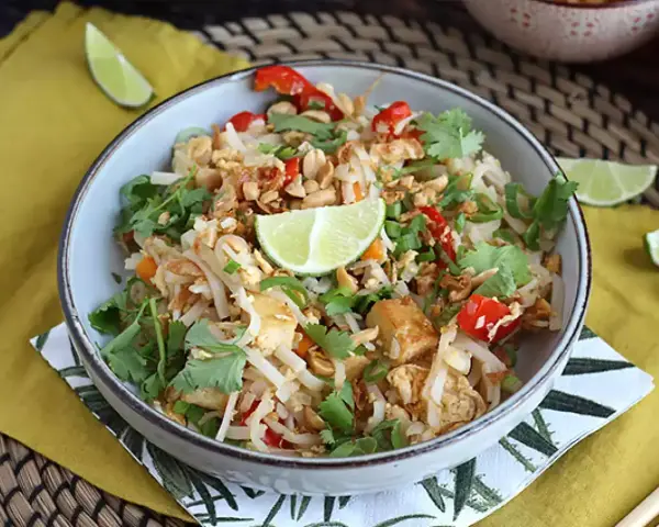 Pyszne pad thai z tofu, posypane orzeszkami ziemnymi i świeżą kolendrą, z kawałkami limonki.