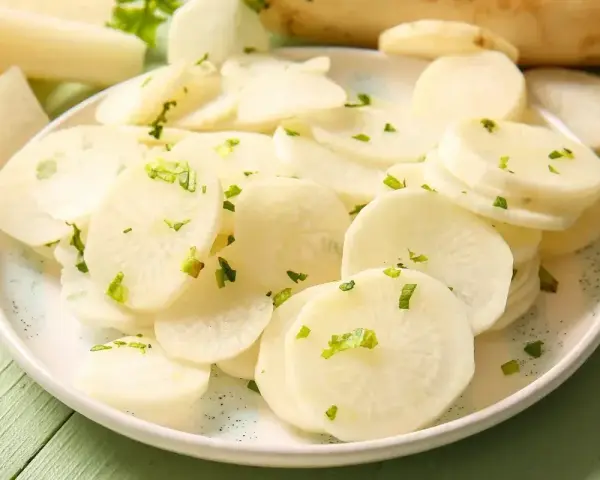 Plasterki białej rzodkwi, czyli daikon, posypane zielonymi ziołami na talerzu.