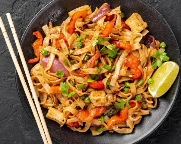 Talerz pełen Pad Thai: makaron ryżowy, tofu, papryka, cebula, groszek i kolendra. Idealny sposób, by dowiedzieć się, pad thai co to.