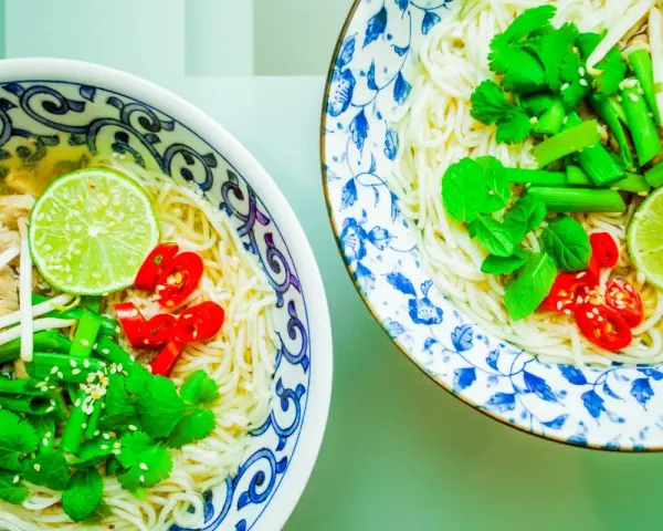 Dwie miseczki aromatycznej zupy pho z makaronem, mięsem, kiełkami, limonką, chili i świeżymi ziołami.