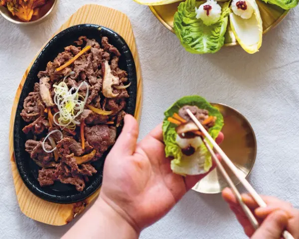 Pyszne bulgogi przepis na talerzu. Ktoś właśnie przygotowuje idealny kęs w liściu sałaty.