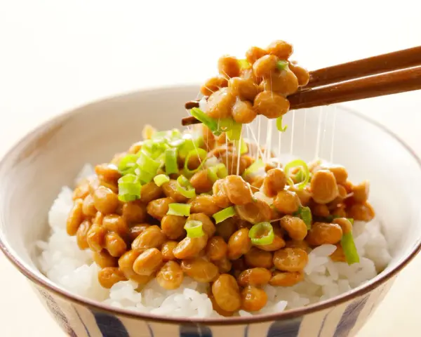 Miseczka ryżu z natto, japońską potrawą z fermentowanej soi, posypana szczypiorkiem. Pałeczki unoszą nitki natto.