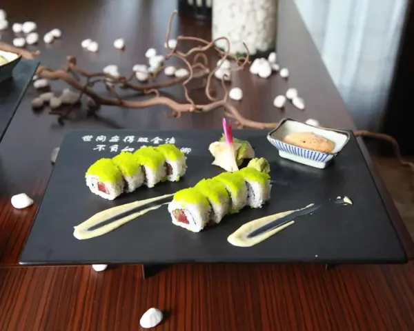 Dwa rzędy sushi z zielonym ikrą, podane z sosem i imbirem. Idealny sposób, jak podawać sushi na eleganckim talerzu.