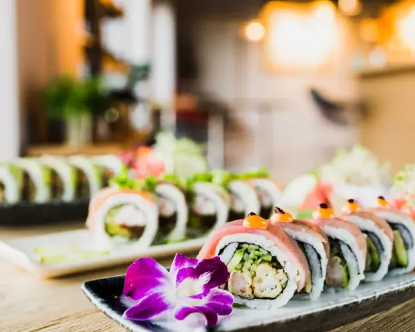 Wykwintne sushi z mięsem, ozdobione kwiatem i warzywami, prezentuje się apetycznie na talerzu.