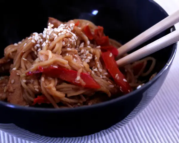 Miseczka pełna aromatycznego makaronu teriyaki z kawałkami kurczaka i papryką, posypana sezamem.