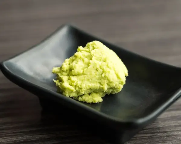 Zielona pasta wasabi na czarnej, kwadratowej miseczce. Zastanawiasz się wasabi co to? To ostry japoński chrzan.