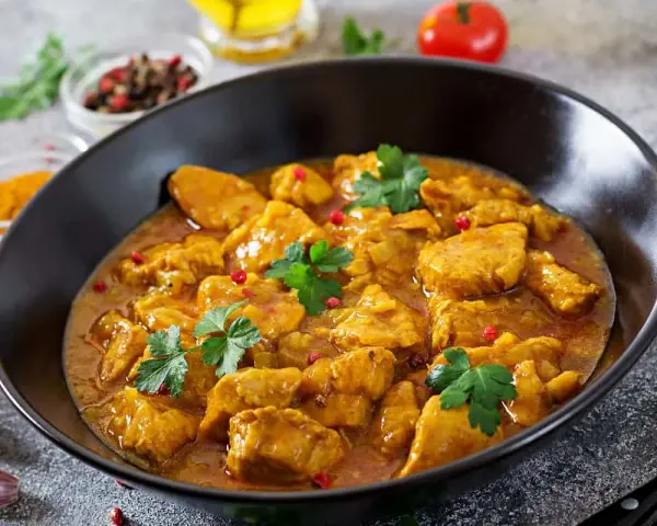 Aksamitny kurczak w sosie curry, jedno z popularnych potraw kuchni azjatyckiej, ozdobiony natką pietruszki i różowym pieprzem.