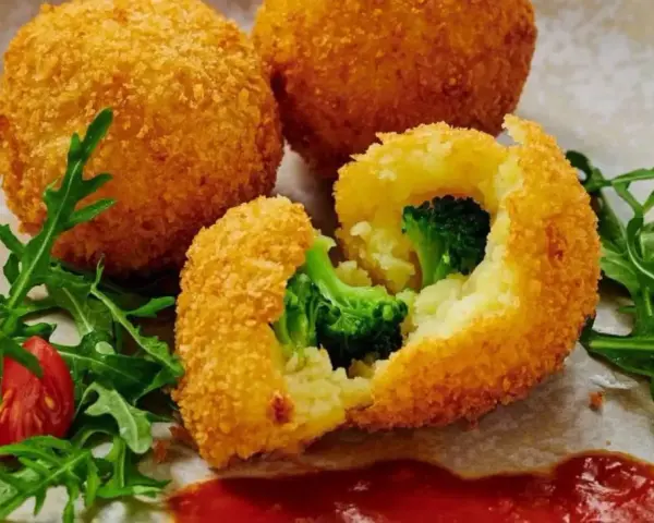 Chrupiące kulki ziemniaczane w panko z brokułami w środku, podane z rukolą i pomidorkami.