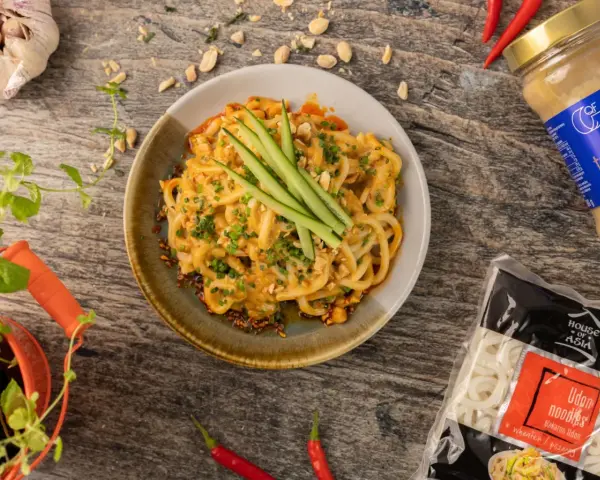 Udon co to? Makaron udon w kremowym sosie z orzeszkami ziemnymi i ogórkiem, obok paczka makaronu i tahini.