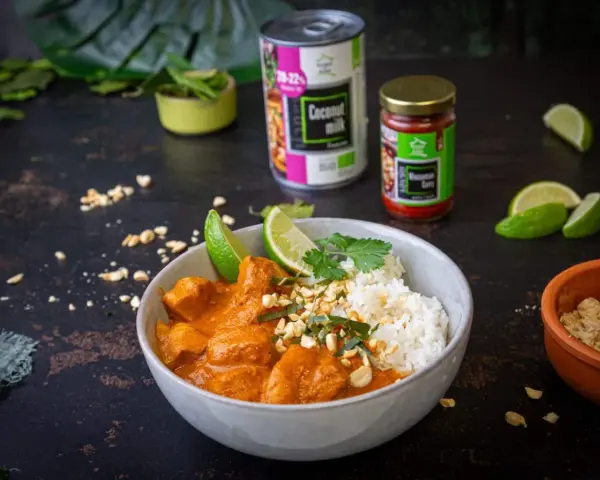 Aksamitny kurczak w sosie massaman curry, podany z ryżem, limonką i posypany orzeszkami. Obok puszka mleka kokosowego i słoiczek pasty massaman.