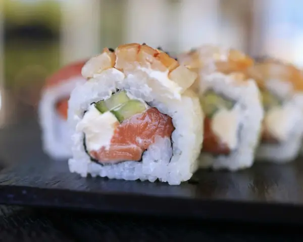 Uramaki co to? Rolka sushi z łososiem, awokado i krewetką, ryż na zewnątrz, na czarnej desce.