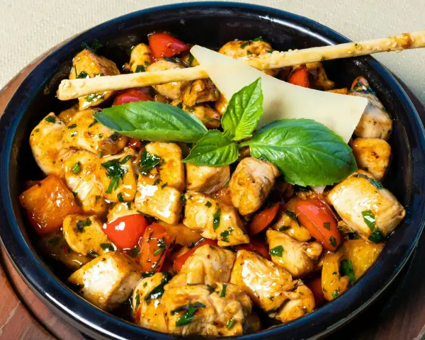 Kawałki kurczaka w sosie z papryką i ziołami, ozdobione listkami bazylii i paluszkami grissini. Danie przypomina egzotyczne jungle curry.
