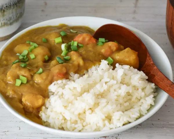 Pyszne japońskie curry z kurczakiem i warzywami, podane z ryżem i posypane szczypiorkiem.